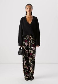 Schwarzer, flauschiger Pullover mit tiefem V-Ausschnitt, kombiniert mit hochtaillierten Blumentrachten, die einen schwarzen Stoffgrund und mehrfarbige Blumenmuster aufweisen.
