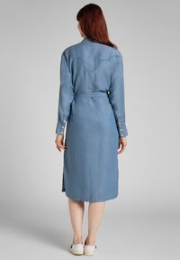 Denim mekko vaaleansinisessä, jossa on pitkät hihat, vyötäröllä vyö, sivurei'itykset ja lännen tyyliin ommeltu sauma takakauluksella.