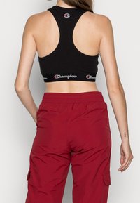 Czarny bawełniany stanik sportowy z dekoltem w kształcie wyścigu i elastycznym pasem z logo. Połączony z czerwonymi spodniami cargo na elastycznym pasku, które mają boczne kieszenie.