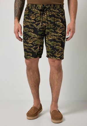 Mand iført shorts med camouflageprint og brune slip-on sko, står med hænderne afslappet ned langs siderne.