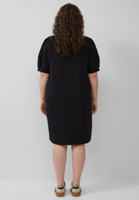 Zwart kortemouwen jurk met een ontspannen pasvorm, knielange zoom en zachte textuur. Gecombineerd met witte en beige sneakers met een metallic accent.