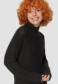 Pull en maille noire à col roulé avec des poignets côtelés et un motif texturé. Le tissu semble épais et chaud, idéal pour les temps plus froids.