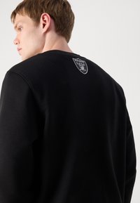 Sweatshirt preto com decote redondo, apresentando um logo gráfico prateado nas costas. Textura suave e corte descontraído.