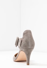 Harmaa mokkanahkainen korkokenkä, jossa on pyöreä kärki, koristeellinen nauha nilkan l�ähellä ja ohut, suppilomainen korko. Sisäpuoli on sileä.