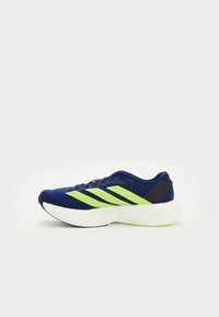 Kék sportcipő lime zöld csíkkal, texturált felsőrész, párnázott bokarész és tömör fehér középtalp, zöld talprészlettel.