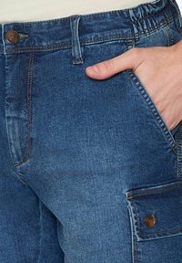 Pantaloni cargo in denim blu con vestibilità rilassata, dotati di chiusura a bottone, tasche laterali e dettagli di cucitura a vista. Tessuto morbido.