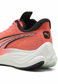 Zapatilla deportiva color coral con parte superior de malla texturizada, detalles en negro y suela blanca. Presenta un talón acolchado y un destacado detalle del logo.