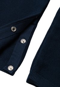 Marineblauer Pullover mit strukturiertem Stoff, Druckknopfverschlüssen und gerippten Kanten für besseren Sitz und Detailverliebtheit. Akzente umfassen Druckknöpfe in Silberoptik.