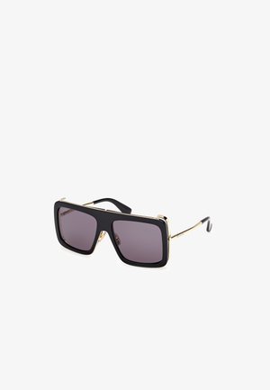 Lunettes de soleil noires surdimensionnées avec des verres teintés foncés, des accents dorés le long du bord supérieur et des branches noires fines. Forme rectangulaire angulaire.