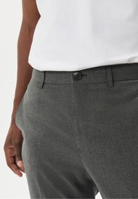 Šedé kalhoty na míru s hladkým povrchem, rovného střihu, s knoflíkovým zapínáním a bočními kapsami, kombinované s bílou klasikou.