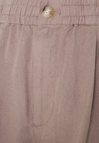 Světle hnědé kalhoty s nařaseným pasem, nefunkčním knoflíkem a jemnými stehmi, se bočními kapsami.