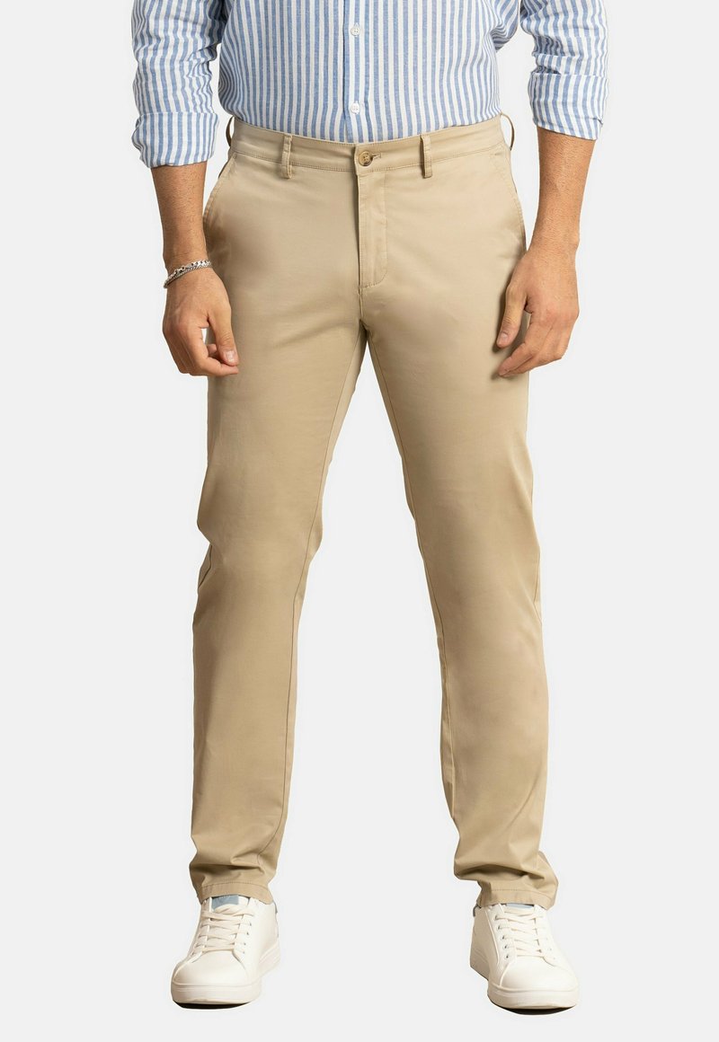 Chinos caqui con una textura suave, que cuentan con bolsillos frontales, cierre de botón y se combinan con zapatillas blancas. Camisa de rayas azules con un patrón.