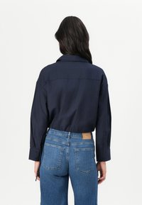 Camisa azul marinho de botão com um corte relaxado, mangas longas e um colarinho largo, combinada com jeans de cintura alta azuis com bolsos traseiros.