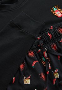 Schwarzer Pullover mit bestickter Flasche Flamin' Hot Sauce und passenden schwarzen Shorts mit Mustern aus roten Chilischoten, Herzen, Getränken und Flaschen mit scharfer Sauce.