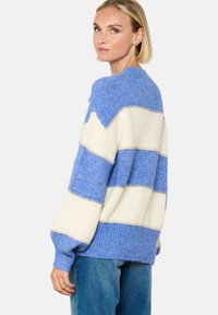 Kootud sviiter siniste ja kreemjate horisontaalsete triipudega, soonikkoes, ümar kaelus ja volüümikad varrukad. Pehme materjal, vabalt lõigatud.