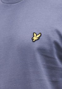 Muška majica s kratkim rukavima od svijetloplavog materijala, na prsima ima zlatno-crni vezeni grb s orlom.