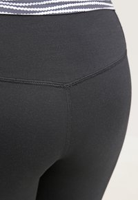 Černé legíny z elastického materiálu, s širokým vzorovaným pasem a hladkými, rovnými švy pro těsný střih.