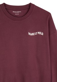 Maroon hoodie van biologische katoen. Heeft een geribbelde ronde hals en een wit 'Marc O’Polo' logo op de borst. Glad van textuur.