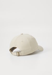Beige színű pamut baseball sapka ívelt csúccsal, állítható pánttal a hátán, és hat panelből álló dizájnnal, amely varrási részletekkel rendelkezik.