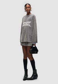 Felpa grigia oversize con grafica bianca, gonna mini houndstooth, calze nere fino al ginocchio e stivaletti neri alla caviglia. Piccola borsa nera in accent.