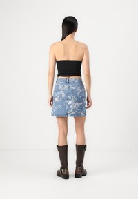 Denim mini krilo s cvetličnim vzorcem, modre barve, zbledele teksture. V kombinaciji z črnim brezrokavnikom in rjavimi usnjenimi škornji do kolen.