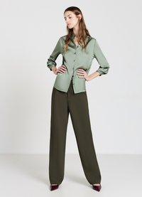 Camicia button-up di raso verde chiaro con una vestibilità rilassata, abbinata a pantaloni a vita alta e a gamba larga verdi oliva e tacchi bordeaux.