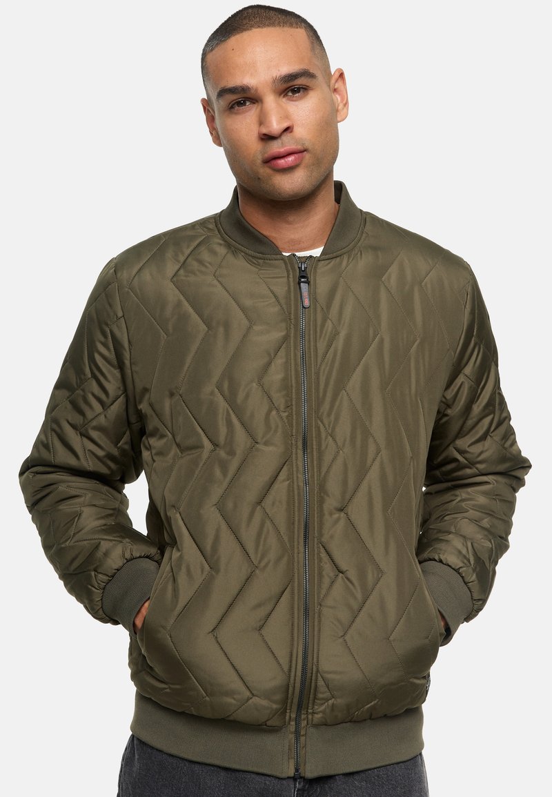 Chaqueta bomber acolchada en verde oliva con cremallera frontal, puños y dobladillo acanalados; presenta un patrón en Chevron y un diseño clásico.