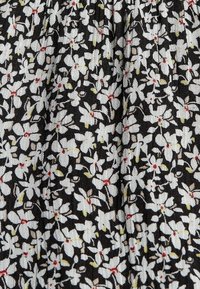 Tissu noir avec un motif dense de petites fleurs blanches, des feuilles jaune-vert, et des centres rouges, montrant la texture et de légers plis.
