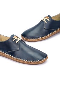 Zapatos de cuero navy con costuras en beige, punta redondeada y un acabado suave. Presentan un diseño de cordones y una suela marrón claro.