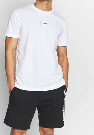 Camiseta de algodón blanca con un pequeño logo negro de Champion en el pecho, combinada con pantalones cortos negros que presentan un logo blanco de Champion en el lateral.