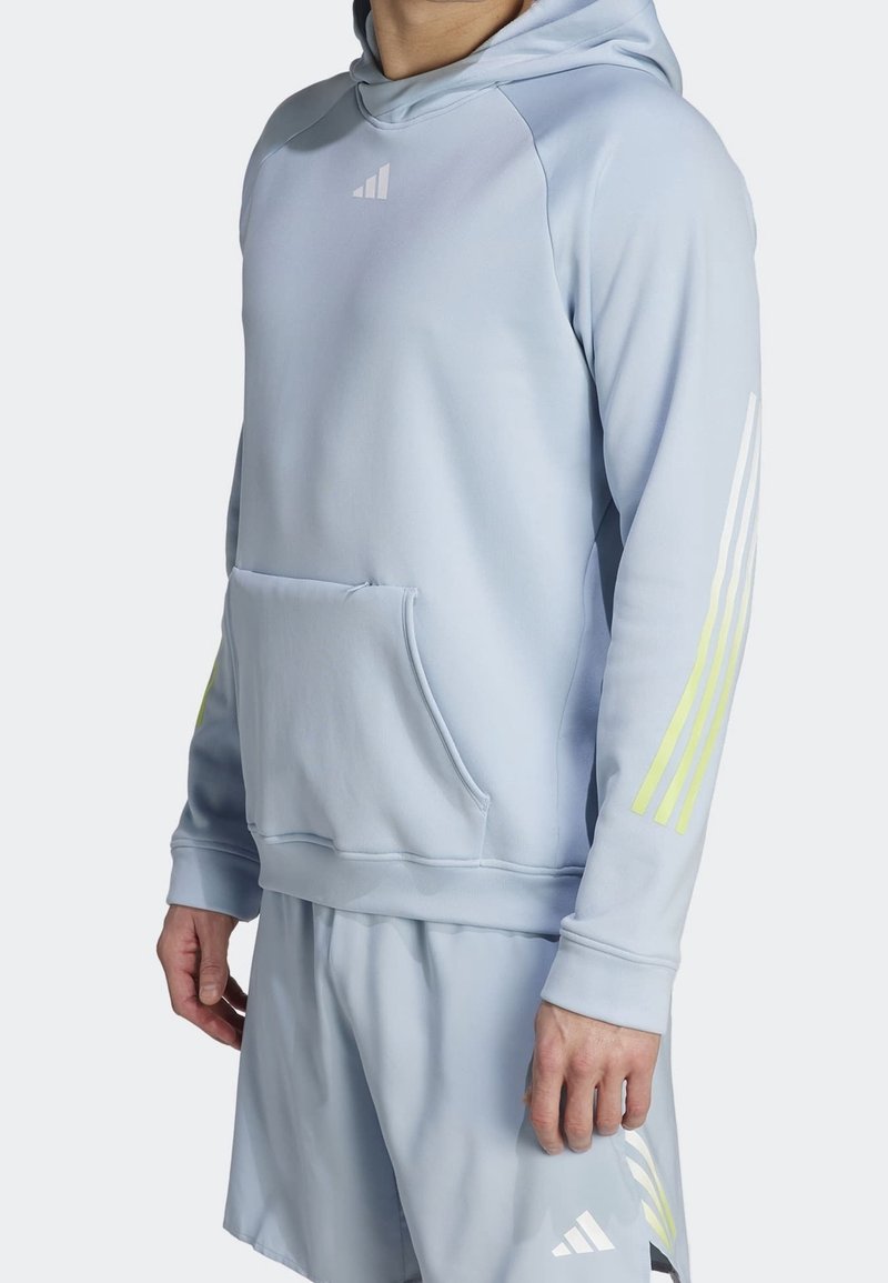 Sweat à capuche bleu clair avec une poche kangourou à l'avant, trois bandes en néon jaune sur la manche droite, et un petit logo blanc sur la poitrine.