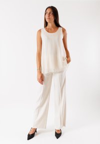 Blusa senza maniche color crema con una vestibilità ampia, abbinata a pantaloni bianchi a gamba dritta. Il modello indossa tacchi a spillo neri. Design minimalista.