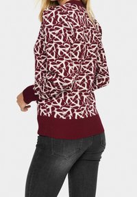 Pull bordeaux avec un motif abstrait blanc, poignets et ourlet côtelés, et une texture tricotée confortable. Vue de dos mettant en valeur les détails du design.
