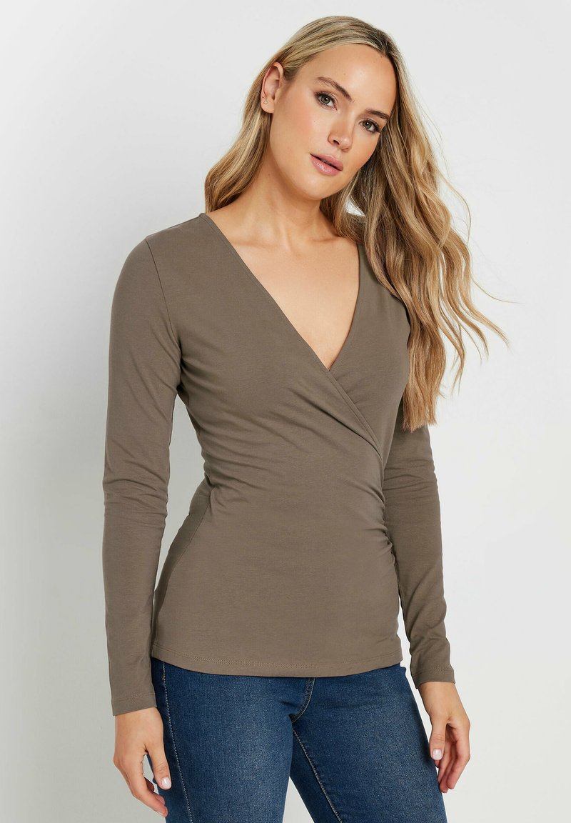 Braunfarbener Langarm-Wickeloberteil mit tiefem V-Ausschnitt, weichem Stoff und tailliertem Design. Kombiniert mit dunkler Denim für einen lässigen Look.