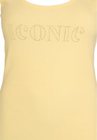 Žlutý žebrovaný top na ramínka s nápisem "ICONIC" vykládaným čirými rhinestony na hrudi. Měkká textura s kulatým výstřihem.