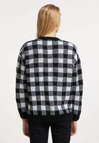 Pulover tricotat cu prindere în carouri alb-negru, cu o croială lejeră, guler și mansete cu zimți. Modelul texturat conferă un aspect tridimensional.