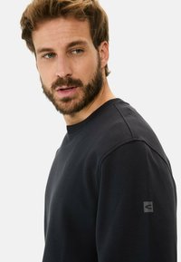 Zwarte sweatshirt met een ronde hals en gestructureerde stof. Een klein logo-opdruk is zichtbaar op de linkermouw.