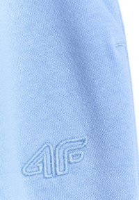 Tissu bleu clair avec gros plan sur le logo brodé en relief "4F" de couleur de fil assortie sur un matériau tricoté texturé.