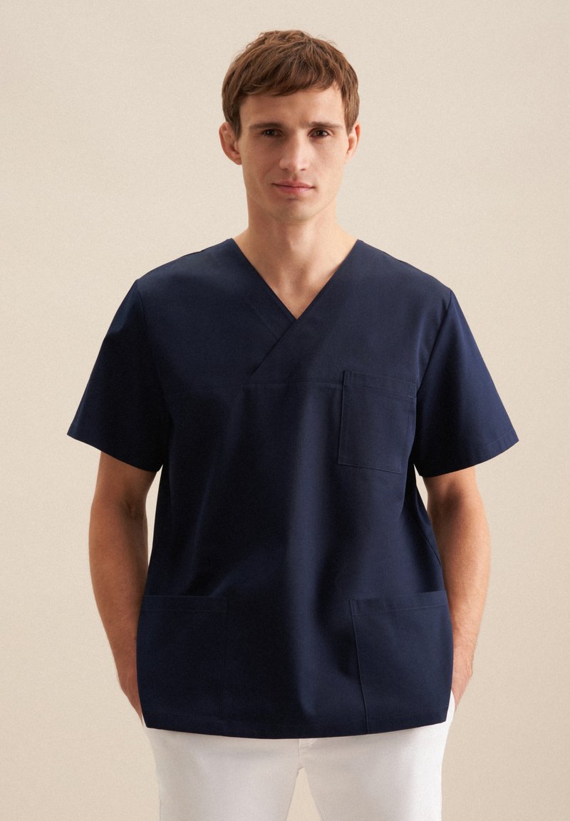 Tunique de scrub bleu marine en tissu durable, avec un col en V, des manches courtes, une poche poitrine et deux poches frontales pour plus de commodité.