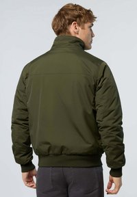 Giacca a vento verde oliva con collo alto, polsini e vita a coste. Presenta una texture liscia e un design semplice senza logo visibile.