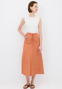 Top sin mangas blanco combinado con una falda de cuadros naranja y blanca hasta la rodilla, con una cinturilla fruncida y lazo ajustable. Sandalias marrones.