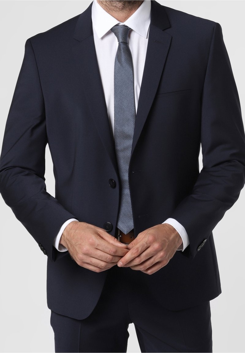 Marineblaues, maßgeschneidertes Sakko mit zwei Knöpfen, Reverskragen und einer Brusttasche, kombiniert mit einer hellblauen gemusterten Krawatte und einem weißen Hemd.