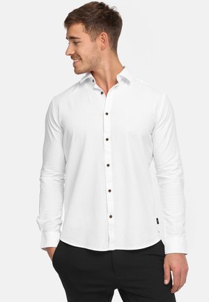 White long-sleeve shirt with a button-down collar, featuring brown buttons, a smooth texture, and a curved hem, paired with black pants.