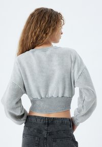 Sudadera gris recortada con un acabado suave y texturizado. Presenta un amplio cuello redondo, mangas abullonadas y un dobladillo acanalado.