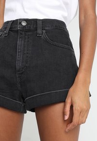 High-waisted black denim shorts with rolled hems, front pockets, and contrasting stitching, featuring a front button closure.