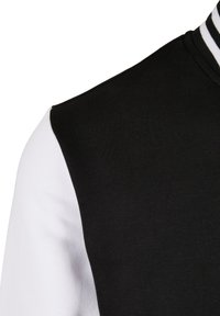 Zwart-wit gekleurde sportjas met blokken, voorzien van een geribde kraag en een gladde textuur, waarbij de contrasterende materialen in de mouwen worden benadrukt.