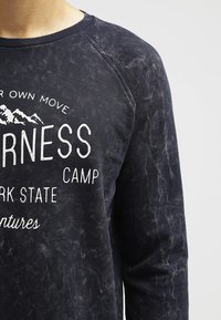 Felpa blu navy con finitura testurizzata, caratterizzata da testo stampato bianco e grafiche di montagne. Collo a costine e maniche raglan.