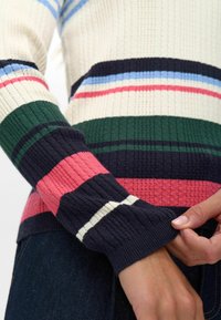 Ženska pletena jopica z rebrastim vzorcem, ki ima pisan vodoravni trakovi v temno modri, zeleni, roza in beli barvi. Poudarek na detajlih rokavov in prileganju.