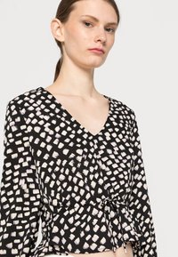Blusa preta com decote em V, mangas longas e bainha franzida com laços. Com padrão de pinceladas brancas e lavanda irregulares.