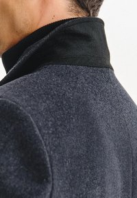 Ciemnoszary płaszcz z mieszanki wełny z czarnym kołnierzem i teksturowaną tkaniną, pokazujący zbliżenie tyłu i projektu dekoltu.